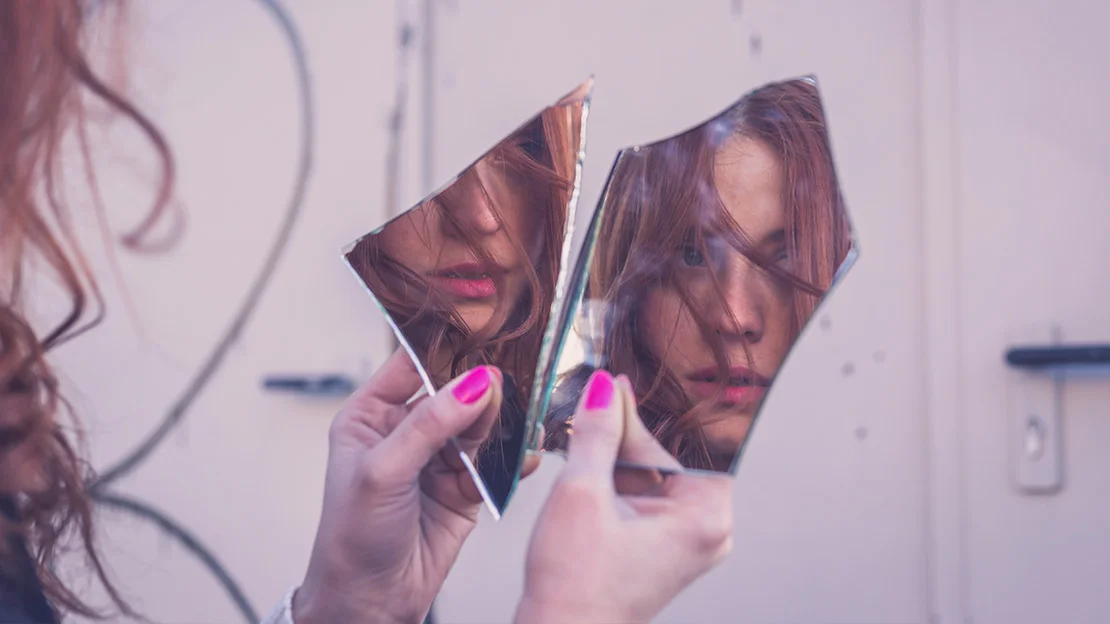 Mulher olhando seu reflexo em um espelho quebrado