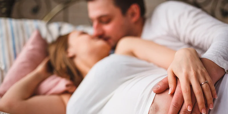 Homem e mulher se beijando, segurando a barriga de grávida